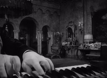 Movie still from “Sunset Blvd.” (1950), directed by Billy Wilder – A person playing the piano in a living room; Medium shot, Low angle