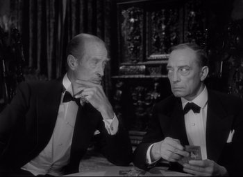 Movie still from “Sunset Blvd.” (1950), directed by Billy Wilder – Two men in tuxedos are sitting at a table; Medium shot, Over the shoulder angle