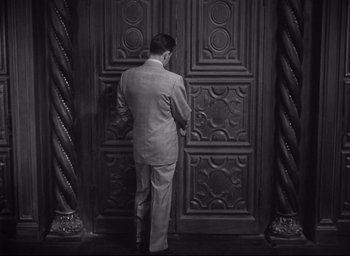 Movie still from “Sunset Blvd.” (1950), directed by Billy Wilder – A black and white photo of a man standing in front of a door; Medium shot, High angle