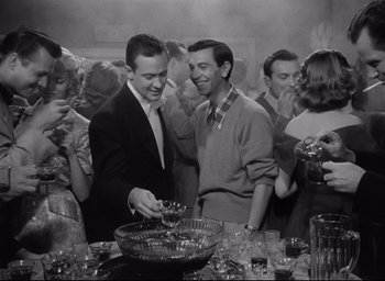 Movie still from “Sunset Blvd.” (1950), directed by Billy Wilder – A group of people standing around a table with drinks on it; Medium shot, High angle