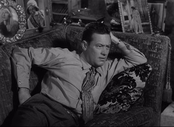 Movie still from “Sunset Blvd.” (1950), directed by Billy Wilder – A black and white photo of a man sitting on a couch; Medium shot, High angle
