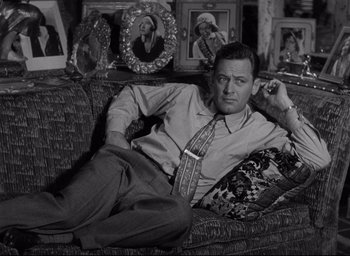 Movie still from “Sunset Blvd.” (1950), directed by Billy Wilder – A black and white photo of a man sitting on a couch; Medium shot, High angle