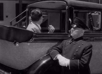Movie still from “Sunset Blvd.” (1950), directed by Billy Wilder – An old photo of a man sitting in the driver's seat of an old car; Medium shot, Low angle