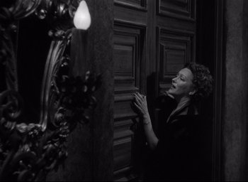 Movie still from “Sunset Blvd.” (1950), directed by Billy Wilder – A black and white photo of a woman standing in front of a door; Medium shot, Low angle