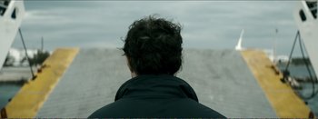 Movie still from “Suntan” (2016), directed by Argyris Papadimitropoulos – A man with curly black hair is looking out at the ocean; Close Up shot, Over the shoulder angle