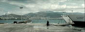 Movie still from “Suntan” (2016), directed by Argyris Papadimitropoulos – A person sitting on the ground near a body of water; Extreme Wide shot, High angle