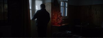 Movie still from “Suntan” (2016), directed by Argyris Papadimitropoulos – A man standing in front of a christmas tree looking out of a window; Wide shot, Low angle