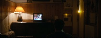 Movie still from “Suntan” (2016), directed by Argyris Papadimitropoulos – A man sitting in front of a tv in a room; Medium shot, Over the shoulder angle