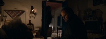 Movie still from “Suntan” (2016), directed by Argyris Papadimitropoulos – A man sitting in front of an open door in a dark room; Medium shot, Over the shoulder angle