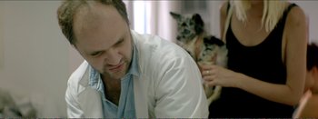 Movie still from “Suntan” (2016), directed by Argyris Papadimitropoulos – A man in a lab coat holding a dog; Medium shot, Over the shoulder angle