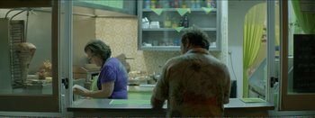 Movie still from “Suntan” (2016), directed by Argyris Papadimitropoulos – A man and a woman sitting at a counter in a kitchen; Medium shot, Over the shoulder angle