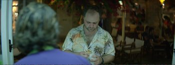 Movie still from “Suntan” (2016), directed by Argyris Papadimitropoulos – A man sitting at a table looking at his cell phone; Medium shot, Over the shoulder angle