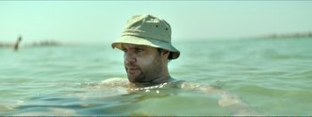 Movie still from “Suntan” (2016), directed by Argyris Papadimitropoulos – A man wearing a hat in the water; Close Up shot, Low angle