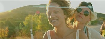 Movie still from “Suntan” (2016), directed by Argyris Papadimitropoulos – A woman smiles while standing in front of some trees; Close Up shot, Low angle