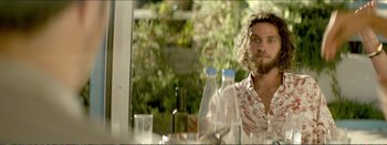 Movie still from “Suntan” (2016), directed by Argyris Papadimitropoulos – A man sitting at a table with a bottle of wine; Medium shot, Over the shoulder angle