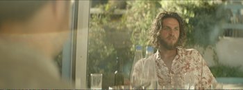 Movie still from “Suntan” (2016), directed by Argyris Papadimitropoulos – A man sitting at a table with a bottle of wine; Medium shot, Low angle