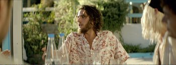 Movie still from “Suntan” (2016), directed by Argyris Papadimitropoulos – A man with long hair and a beard is sitting at a table; Medium shot, Over the shoulder angle