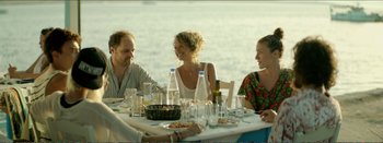 Movie still from “Suntan” (2016), directed by Argyris Papadimitropoulos – A group of people sitting at a table with food; Medium shot, Over the shoulder angle