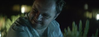 Movie still from “Suntan” (2016), directed by Argyris Papadimitropoulos – A man smiling for the camera; Close Up shot, Over the shoulder angle