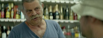 Movie still from “Suntan” (2016), directed by Argyris Papadimitropoulos – An older man with a mustache in front of bottles of wine; Close Up shot, Over the shoulder angle