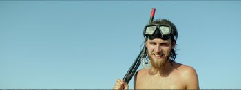 Movie still from “Suntan” (2016), directed by Argyris Papadimitropoulos – A man with a beard wearing goggles and holding a spear; Close Up shot, Low angle
