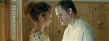 Movie still from “Suntan” (2016), directed by Argyris Papadimitropoulos – A man and a woman staring at each other in front of a wooden wall; Close Up shot, Over the shoulder angle