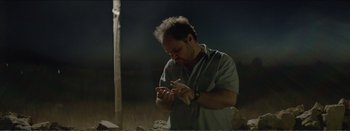 Movie still from “Suntan” (2016), directed by Argyris Papadimitropoulos – A man holding something in his hands while standing in a field; Medium shot, Low angle