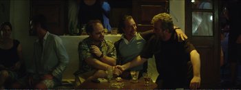 Movie still from “Suntan” (2016), directed by Argyris Papadimitropoulos – A group of men sitting at a table with drinks in front of them; Medium shot, Over the shoulder angle