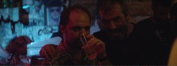 Movie still from “Suntan” (2016), directed by Argyris Papadimitropoulos – Two men are sitting at a bar and one of them is holding a drink; Close Up shot, Over the shoulder angle