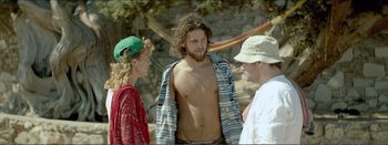 Movie still from “Suntan” (2016), directed by Argyris Papadimitropoulos – A man with long hair is standing next to two other men; Medium shot, Over the shoulder angle