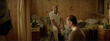 Movie still from “Suntan” (2016), directed by Argyris Papadimitropoulos – A man sitting in front of another man in front of a wooden wall; Medium shot, Over the shoulder angle