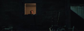 Movie still from “Suntan” (2016), directed by Argyris Papadimitropoulos – A man looking out of a window in a dark room; Medium shot, Over the shoulder angle