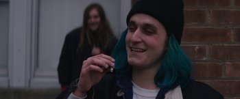 Movie still from “Super Dark Times” (2017), directed by Kevin Phillips – A man with blue hair is holding something in his mouth; Close Up shot, Over the shoulder angle