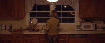 Movie still from “Super Dark Times” (2017), directed by Kevin Phillips – A woman standing at a sink in front of a window; Medium shot, Over the shoulder angle