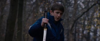 Movie still from “Super Dark Times” (2017), directed by Kevin Phillips – A young man holding a baseball bat while standing in the woods; Close Up shot, Over the shoulder angle