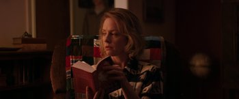 Movie still from “Super Dark Times” (2017), directed by Kevin Phillips – A woman sitting in a chair while reading a book; Medium shot, Over the shoulder angle