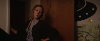 Movie still from “Super Dark Times” (2017), directed by Kevin Phillips – A woman leaning against a wall in a room; Medium shot, Over the shoulder angle