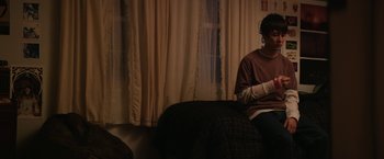 Movie still from “Super Dark Times” (2017), directed by Kevin Phillips – A person sitting on a couch in front of a window; Medium shot, High angle