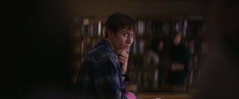 Movie still from “Super Dark Times” (2017), directed by Kevin Phillips – A man sitting in front of a book shelf with his hand under his chin; Close Up shot, Over the shoulder angle