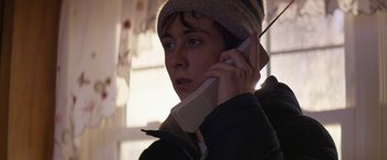 Movie still from “Super Dark Times” (2017), directed by Kevin Phillips – A young man talking on a cell phone while wearing a hat; Close Up shot, Low angle