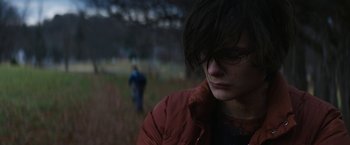 Movie still from “Super Dark Times” (2017), directed by Kevin Phillips – A person wearing a red jacket standing in a field; Close Up shot, Over the shoulder angle