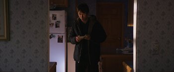 Movie still from “Super Dark Times” (2017), directed by Kevin Phillips – A man standing in a kitchen holding a nintendo wii game controller; Medium shot, Over the shoulder angle