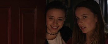 Movie still from “Super Dark Times” (2017), directed by Kevin Phillips – A young woman smiles while standing next to a door; Close Up shot, Over the shoulder angle