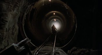 Movie still from “Super Mario Bros.” (1993), directed by Annabel Jankel – A man is walking down a train track in a tunnel; Wide shot, Low angle