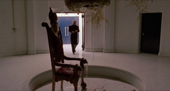 Movie still from “Super Mario Bros.” (1993), directed by Annabel Jankel – A man walking down a hallway next to an old chair; Wide shot, High angle