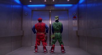 Movie still from “Super Mario Bros.” (1993), directed by Annabel Jankel – Two men in red and green costumes standing in front of a lift; Wide shot, Low angle