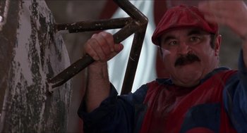 Movie still from “Super Mario Bros.” (1993), directed by Annabel Jankel – A man in a red and blue shirt holding a wooden stick; Close Up shot, Low angle