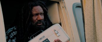 Movie still from “Surrogates” (2009), directed by Jonathan Mostow – A man with a dreadlocks holding a white suitcase; Close Up shot, Low angle