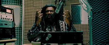 Movie still from “Surrogates” (2009), directed by Jonathan Mostow – A man with a dreadlocks is talking into a microphone in front of him; Medium shot, Low angle