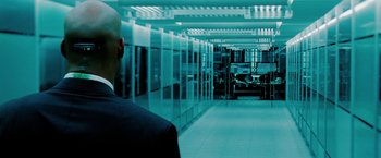 Movie still from “Surrogates” (2009), directed by Jonathan Mostow – A man in a suit and tie in front of a row of computers; Wide shot, Over the shoulder angle